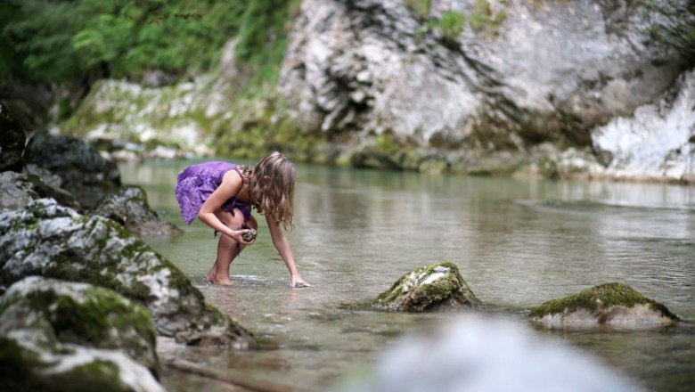 Naturpark Ötscher Tormäuer, © Mostviertel Tourismus, weinfranz.at Ein Kind im lila Kleid spielt in einem klaren Bach, umgeben von Felsen und grüner Natur.