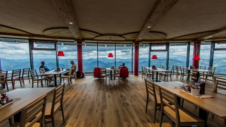 Moderne Hüttenatmosphäre, © Növog/Kerschbaummayr Innenansicht eines modernen Restaurants mit Panoramafenstern und Bergblick.