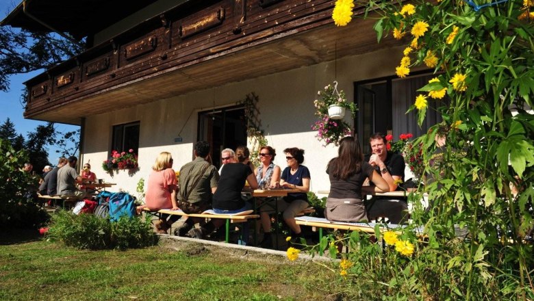 Waldbauernhof, © zVg Gemeinde Annaberg Menschen sitzen an Tischen vor einem Bauernhaus im Freien.
