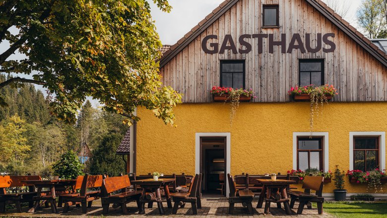 Am Tor zum Naturpark Ötscher-Tormäuer gelegen, © Niederösterreich Werbung/Daniela Führer Ein gelbes Gasthaus mit Holztischen und Bänken im Freien, umgeben von Bäumen und Natur.