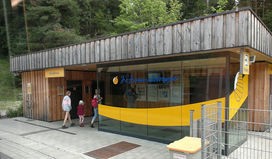 Bahnhof Erlaufklause mit Holzfassade und Glasfront, Menschen betreten das Gebäude.