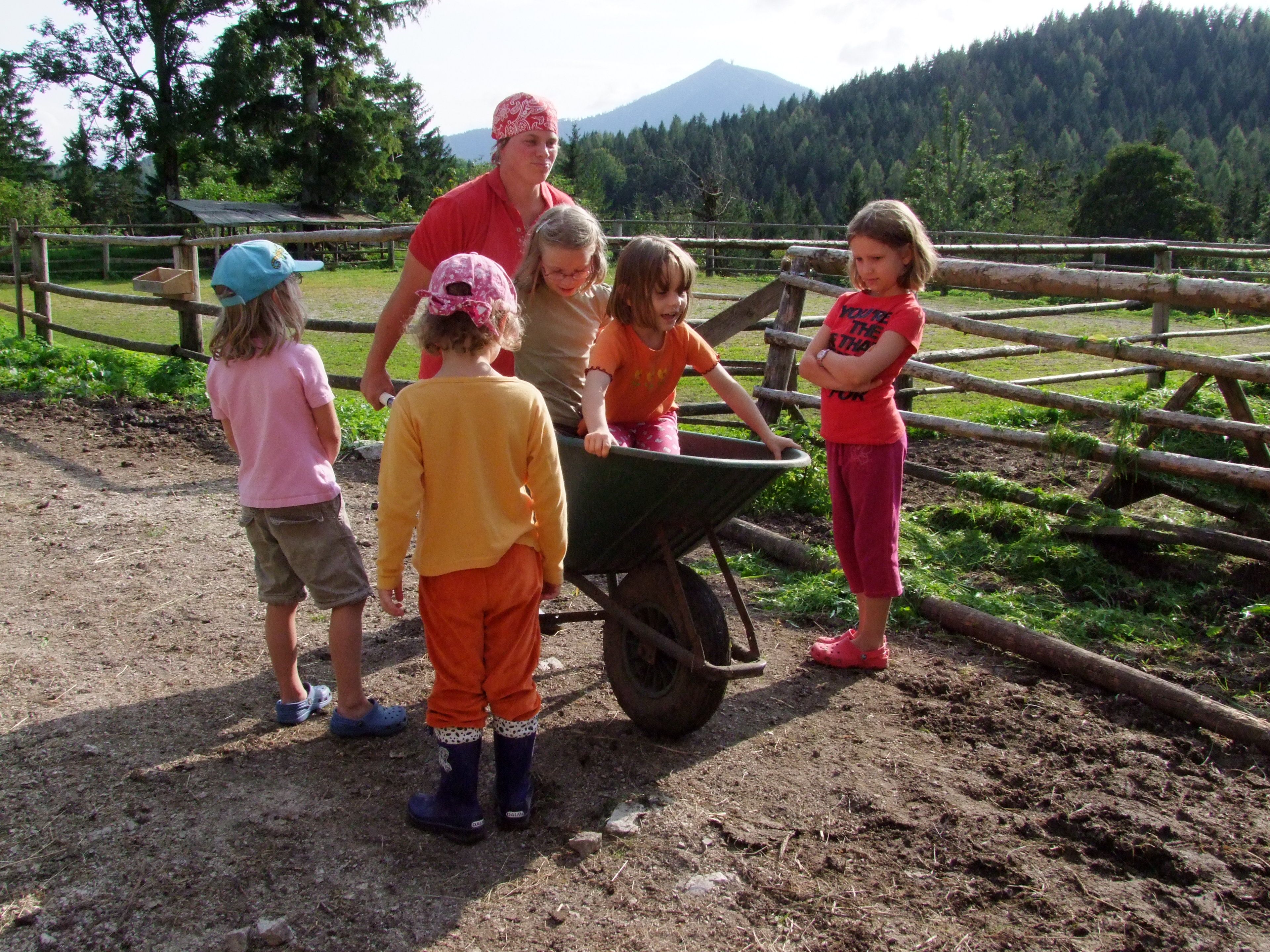Kinder spielen mit einer Schubkarre auf einem Bauernhof.