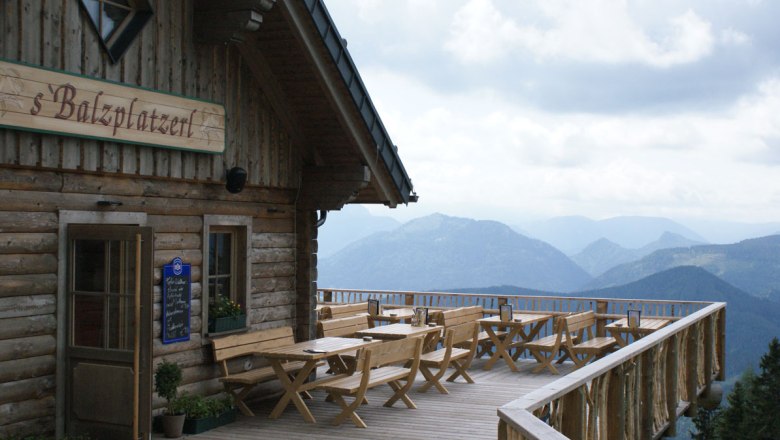 Holzterrasse mit Tischen und B&auml;nken vor einer Bergh&uuml;tte mit Blick auf die Alpen.