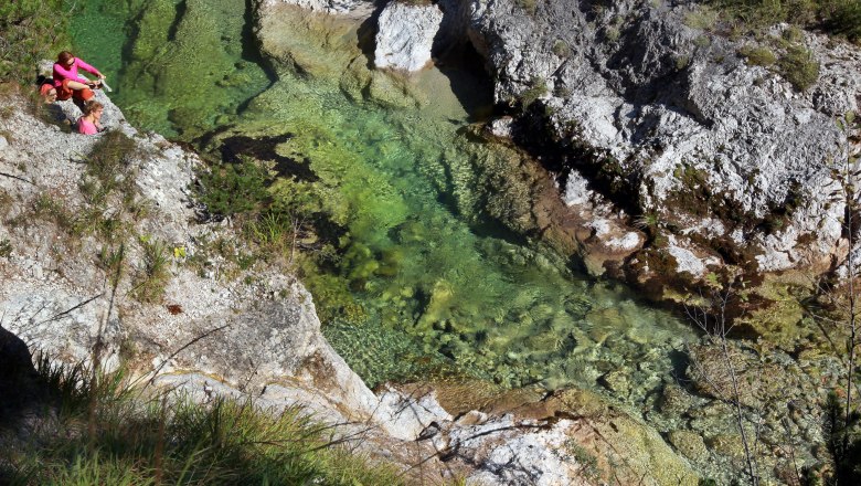Two people are sitting on a rock next to a clear, green river in a gorge.