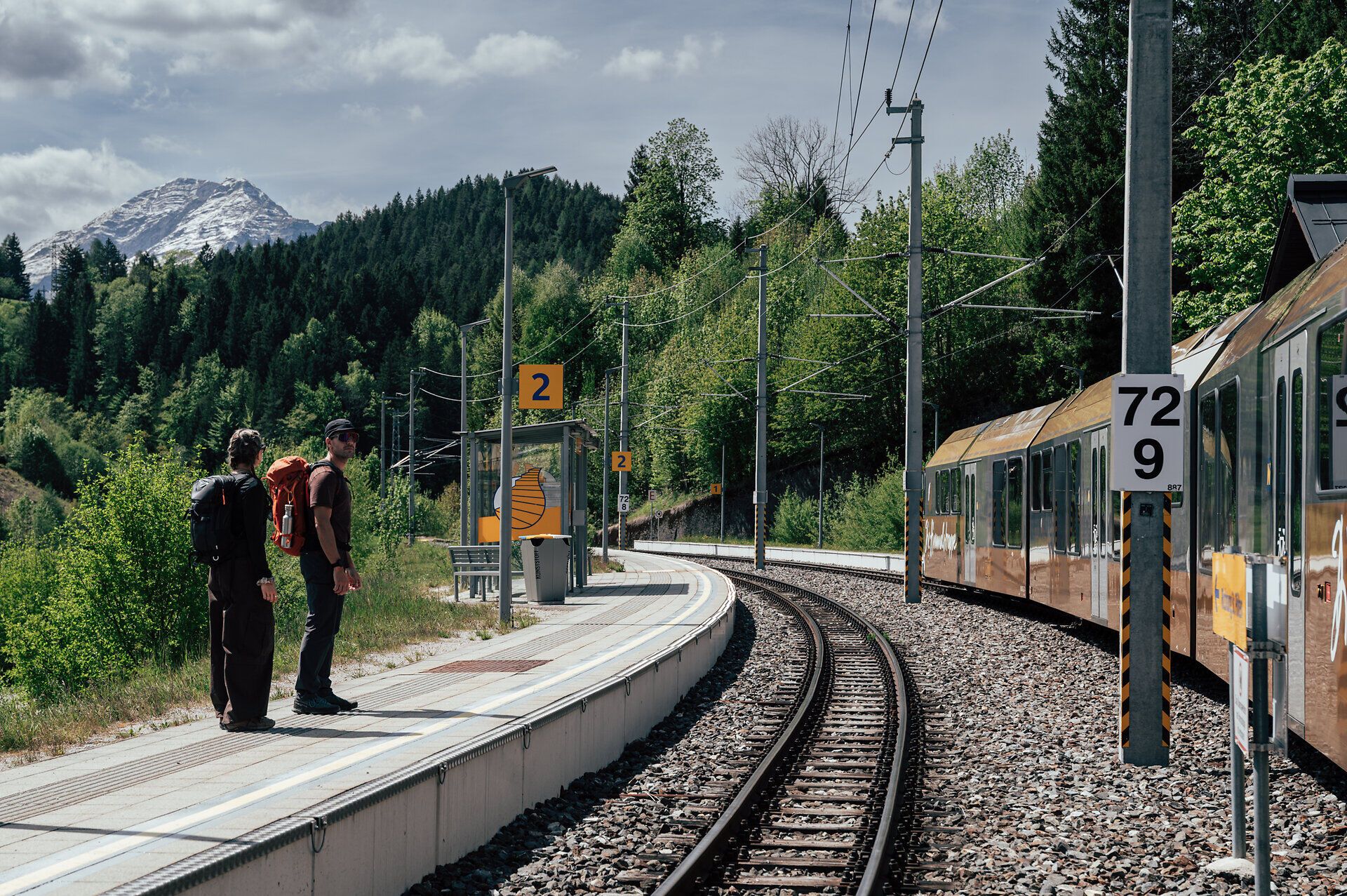 Zwei Wandernde warten mit Blick auf den Ötscher auf die Mariazellerbahn am Luchs Trail.