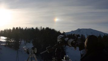 Telescopes on a snowy mountain landscape with solar halo.