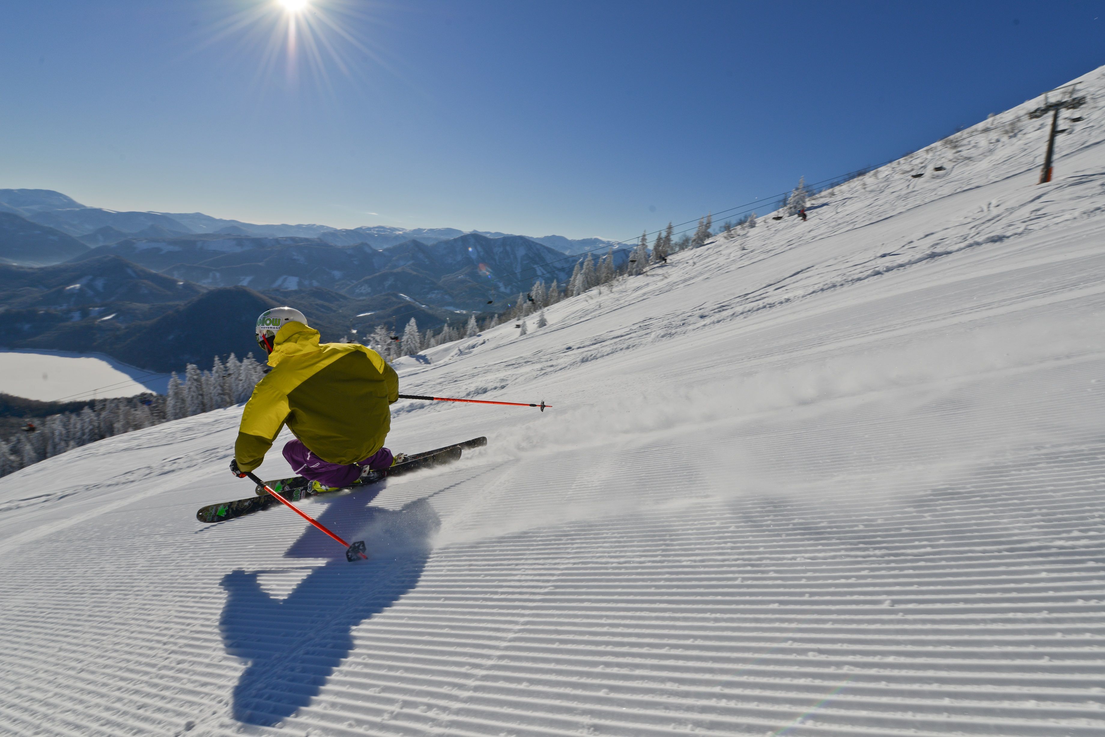 Skifahrer auf einer Piste mit Blick auf den Erlaufsee und Berge im Hintergrund.