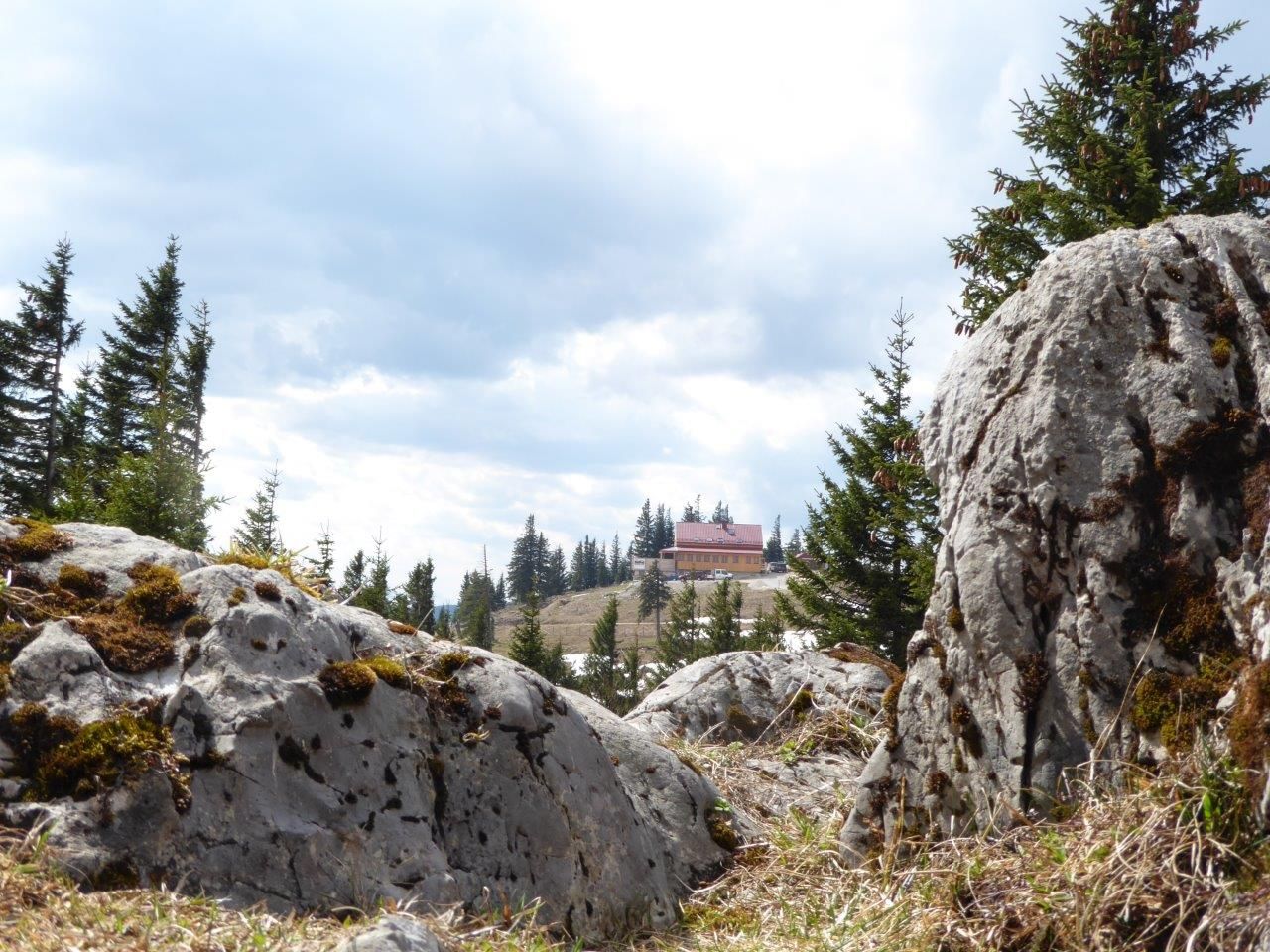 Blick auf das Annabergerhaus in einer Berglandschaft mit Felsen und Bäumen im Vordergrund.