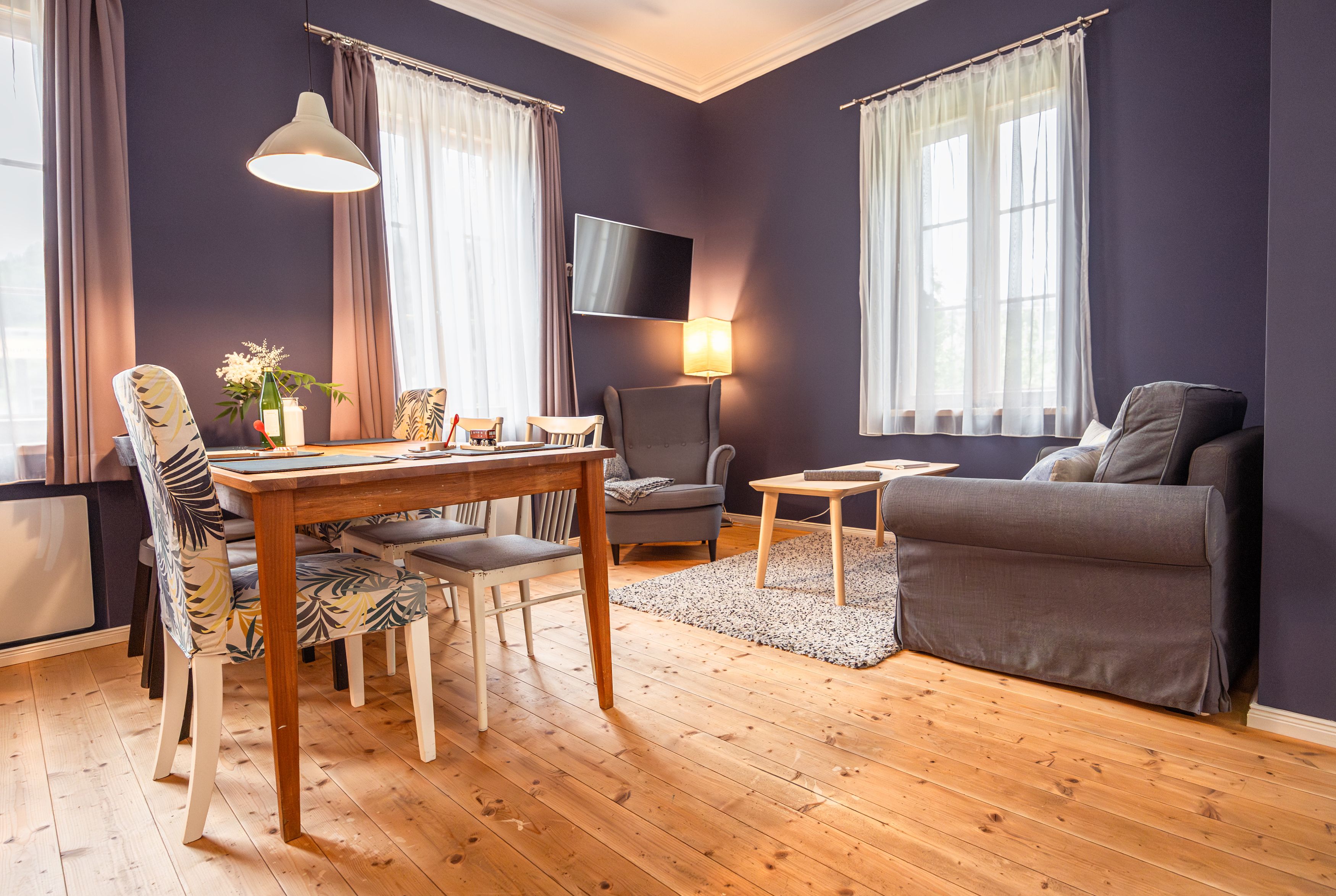 Cozy living room with wooden floor, dining table, chairs, armchair and sofa.