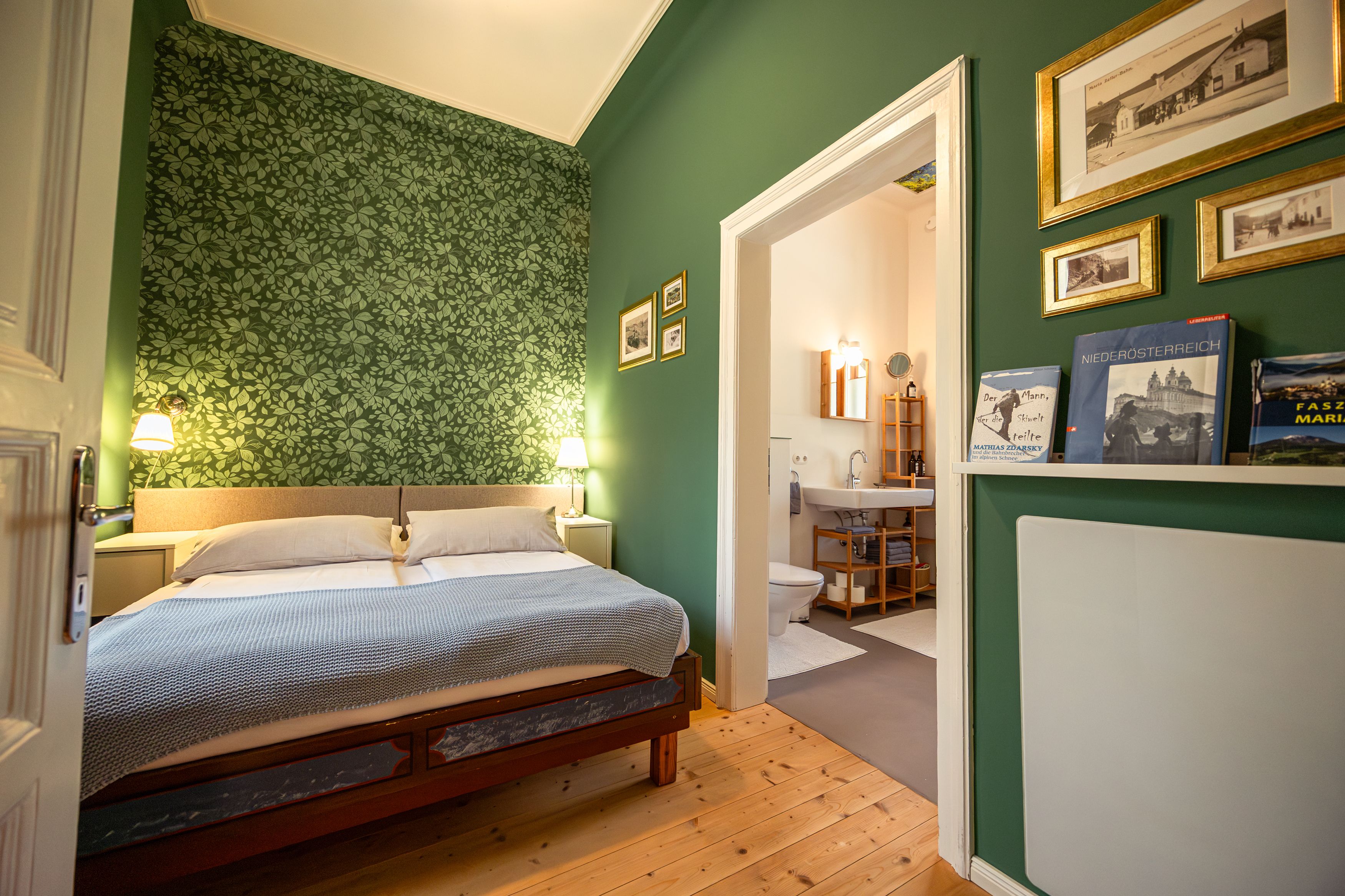 Cozy bedroom with green patterned wallpaper, double bed and adjoining bathroom.