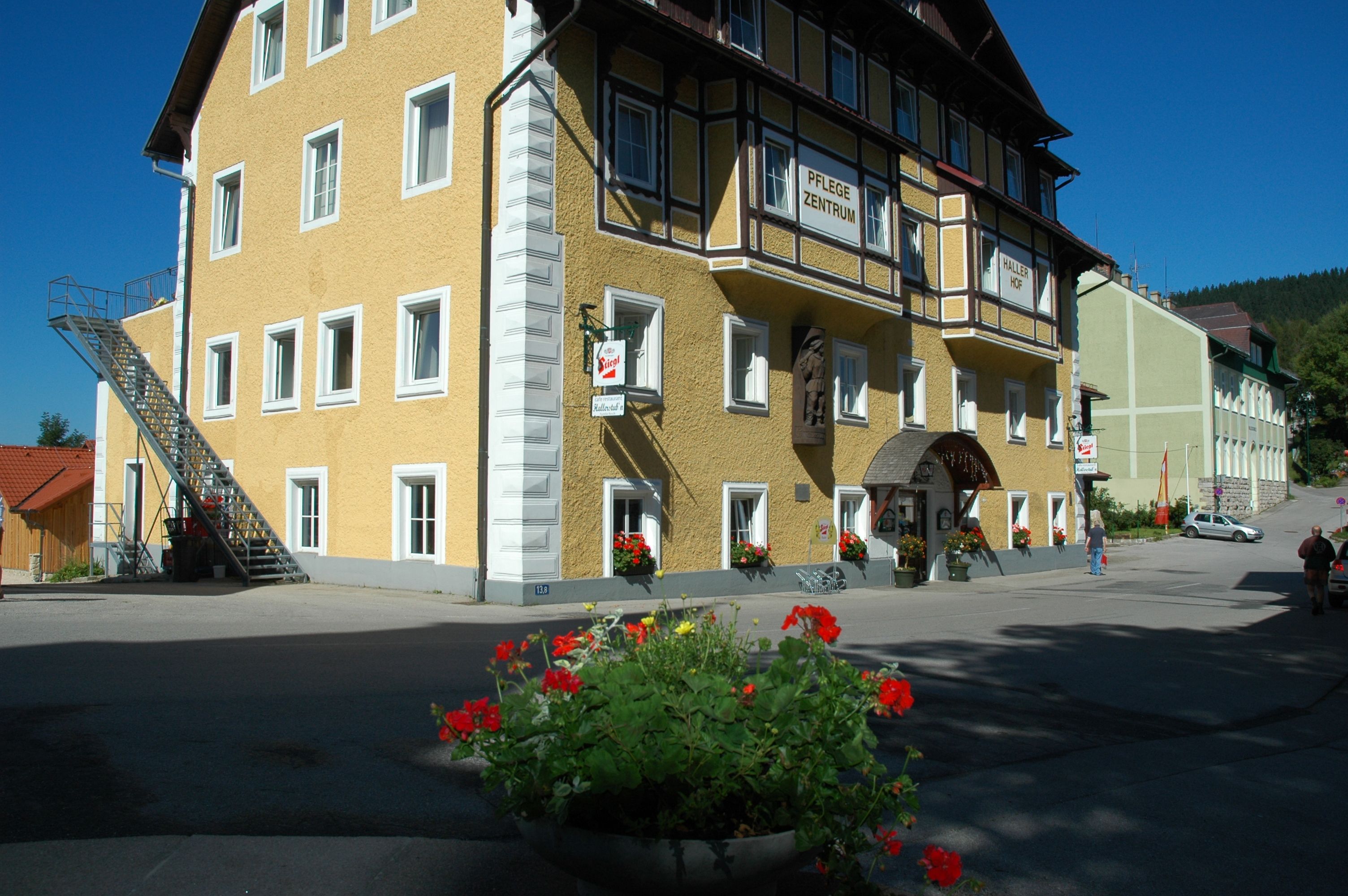 Gelbes Gebäude mit der Aufschrift 'Hallerhof', Blumen im Vordergrund.