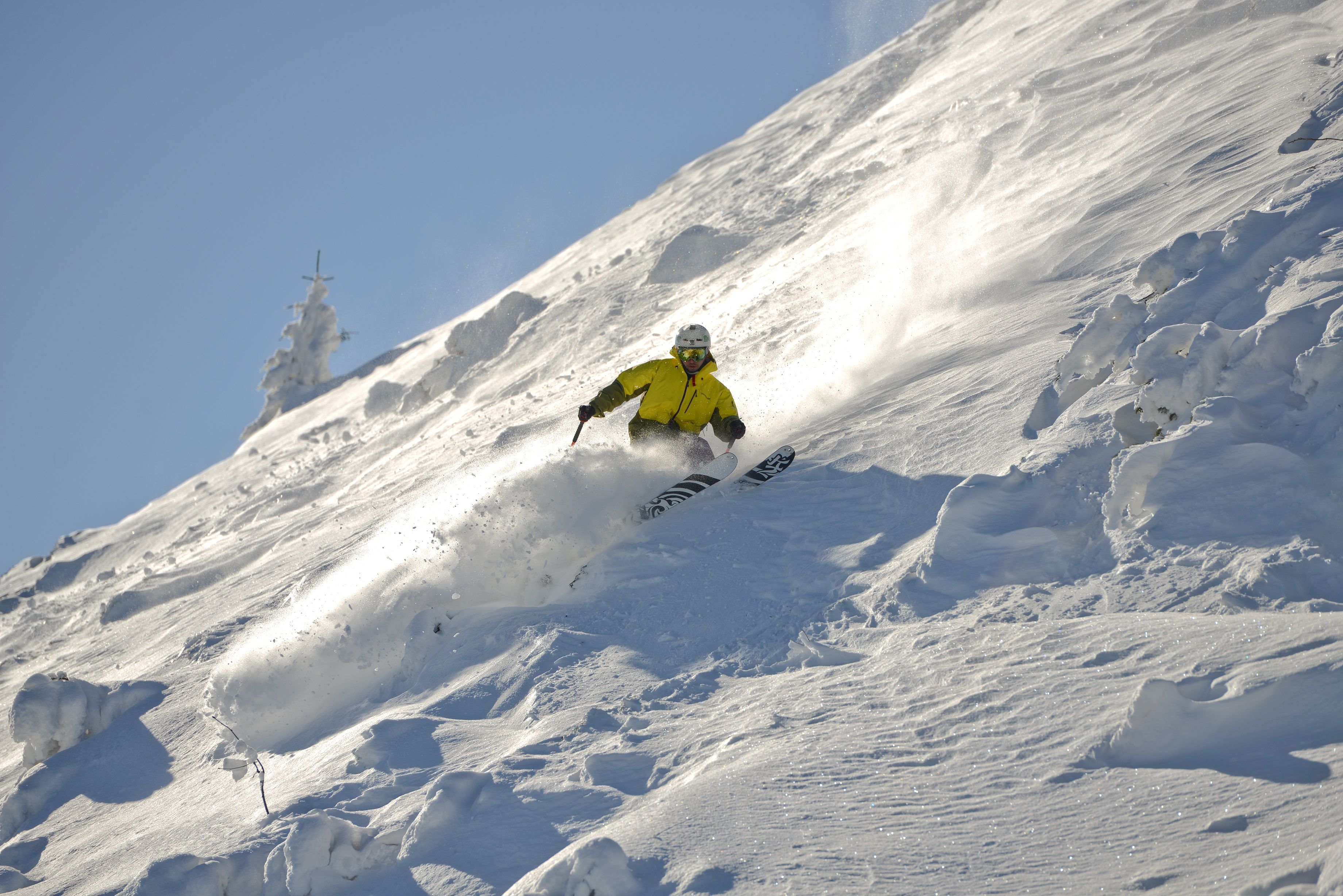Ein Skifahrer in gelber Jacke fährt eine verschneite Piste hinunter.