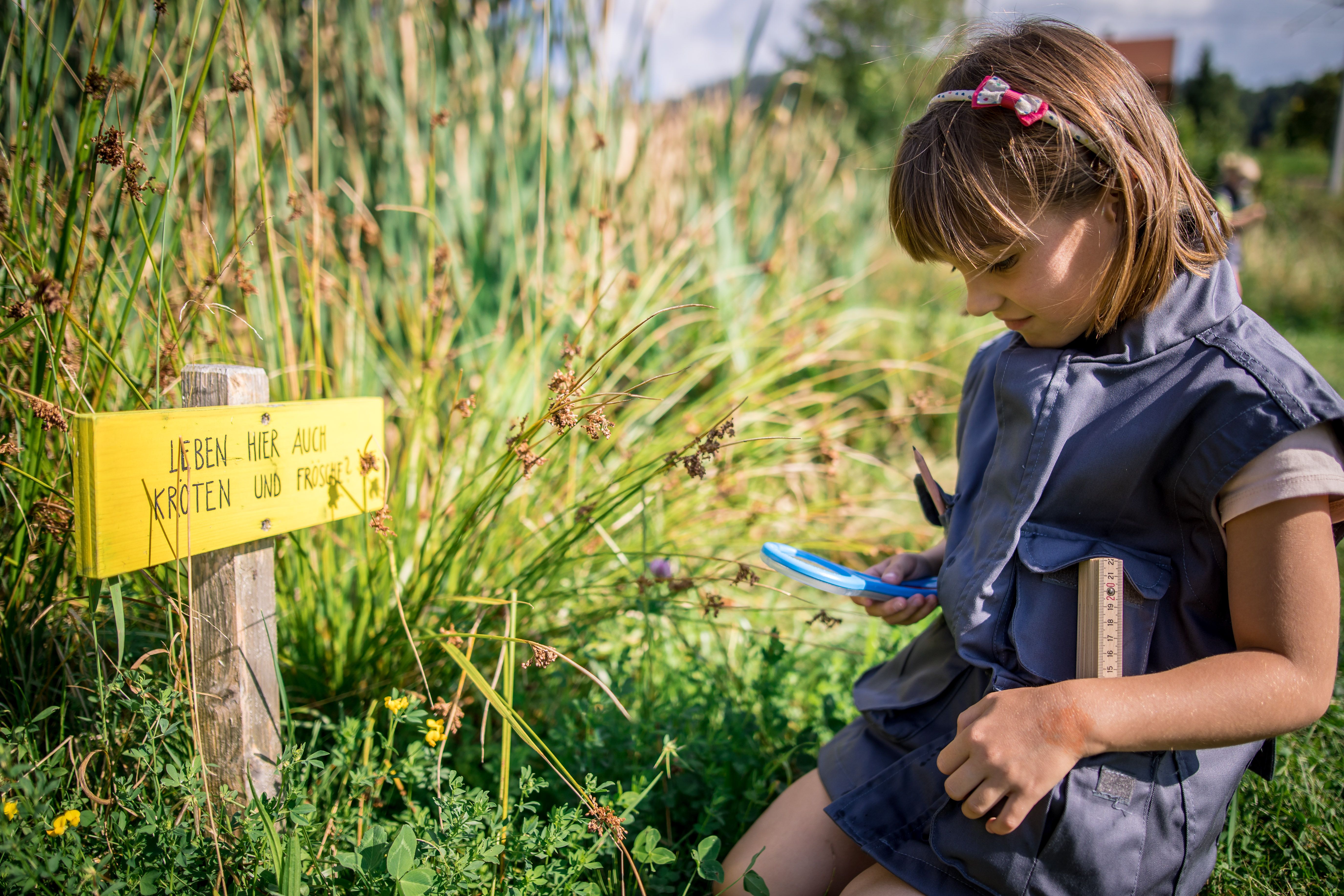 Mädchen kniet mit einer Lupe am Boden und beobachtet