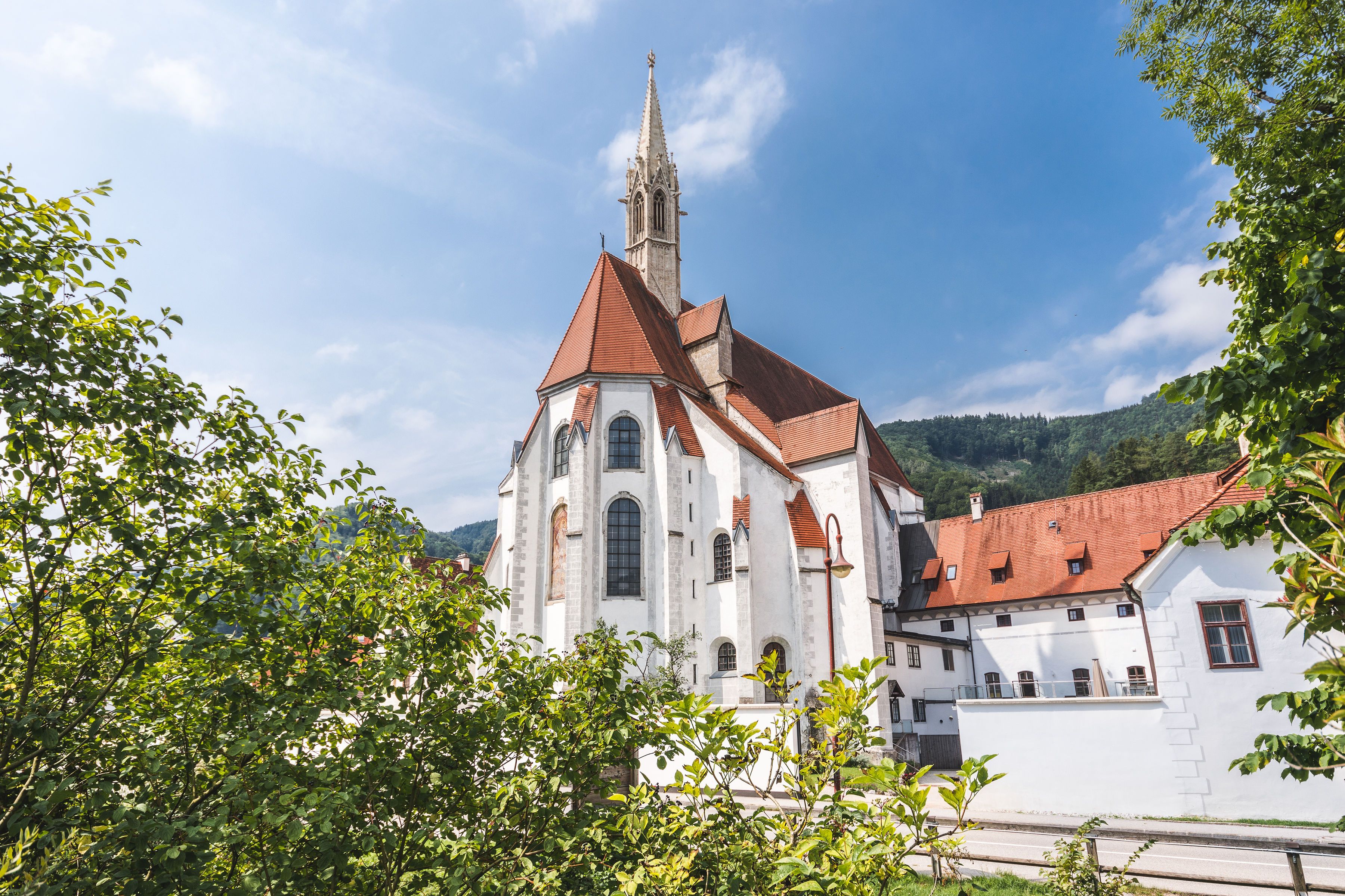 Historisches Gebäude mit rotem Dach und Turm, umgeben von Bäumen.