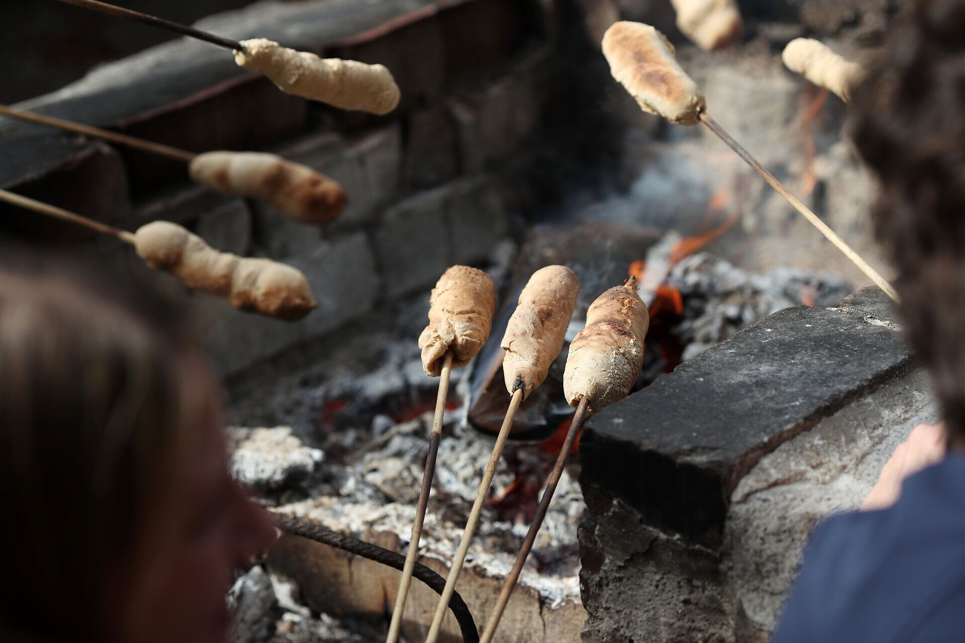 Über einem Grillplatz im Naturpark Sparbach wird von mehreren Leuten Stockbrot gegrillt. 