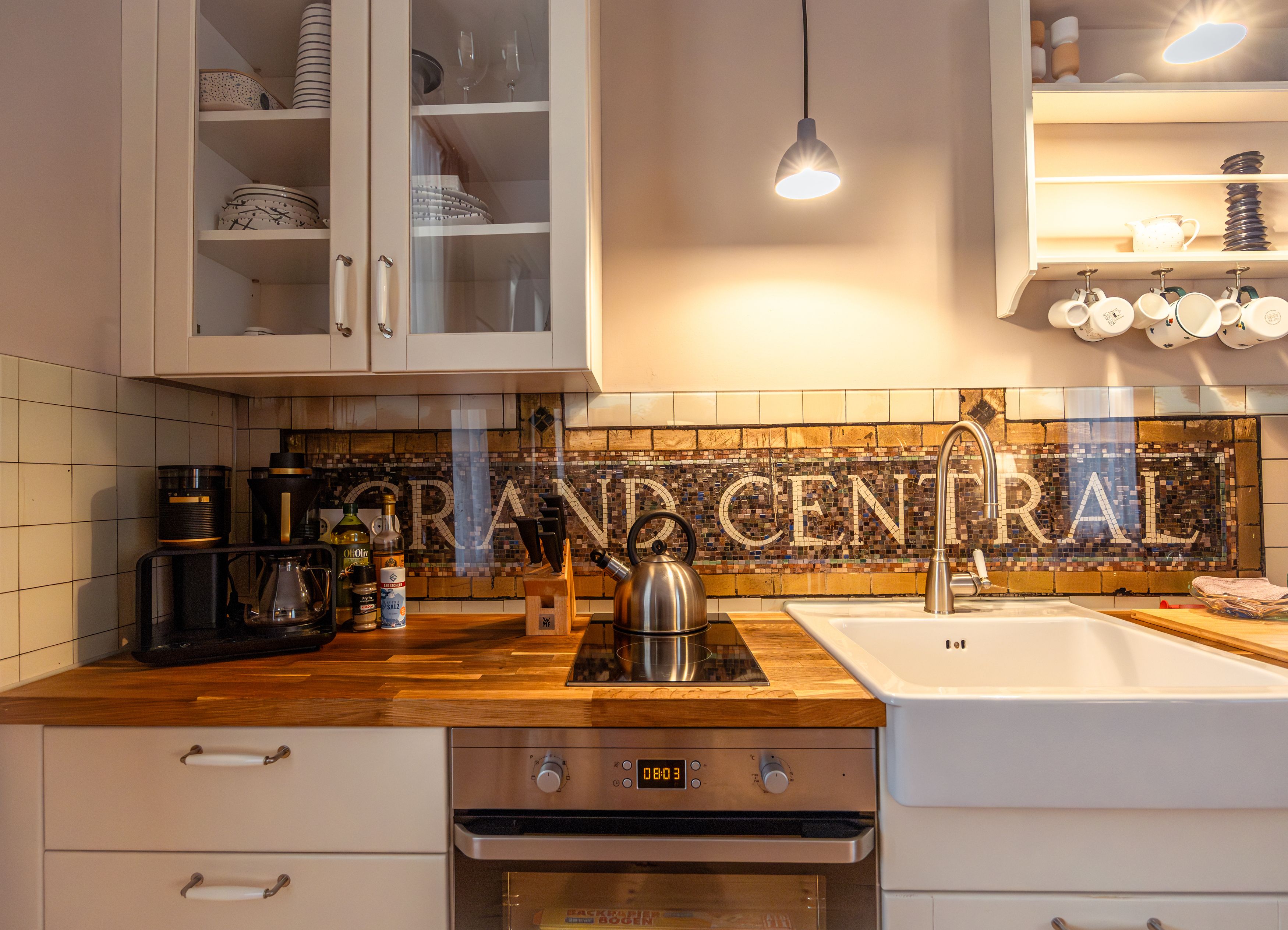 Kitchen with wooden counters, sink, stove and mosaic tiles with 'GRAND CENTRAL'.
