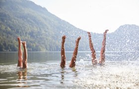 Die warmen Sonnenstrahlen tanzen auf der Wasseroberfl&auml;che, w&auml;hrend fr&ouml;hliche Menschen mit ihren Beinen im klaren Wasser planschen. Umgeben von majest&auml;tischen Bergen und &uuml;ppigem Gr&uuml;n, vermittelt dieser Ort ein Gef&uuml;hl von Freiheit und Lebensfreude. Hier wird der Sommer in seiner sch&ouml;nsten Form erlebt.