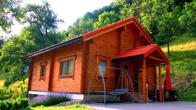 Ein Holzferienhaus mit rotem Dach in einer grünen, bewaldeten Umgebung.