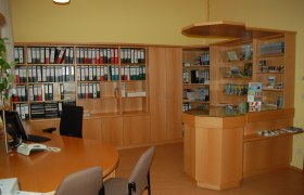 Innenansicht eines Büros mit Holzregalen, Aktenordnern und einem Empfangstresen.