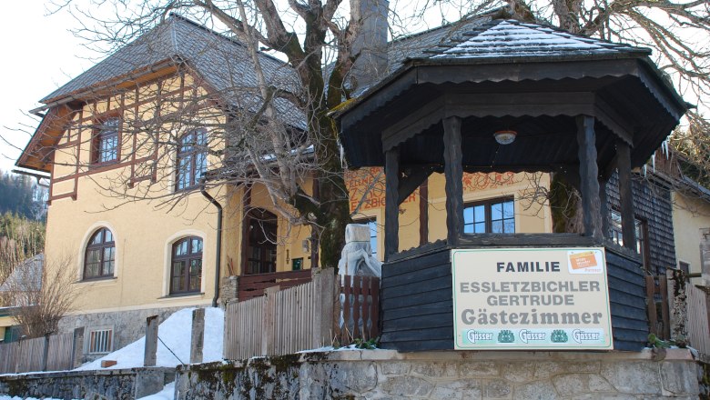 Gelbes Gästehaus mit Holzveranda und Schild 'Familie Essletzbichler Gertrude Gästezimmer'.