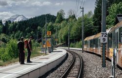 Zwei Wandernde warten mit Blick auf den Ötscher auf die Mariazellerbahn am Luchs Trail.