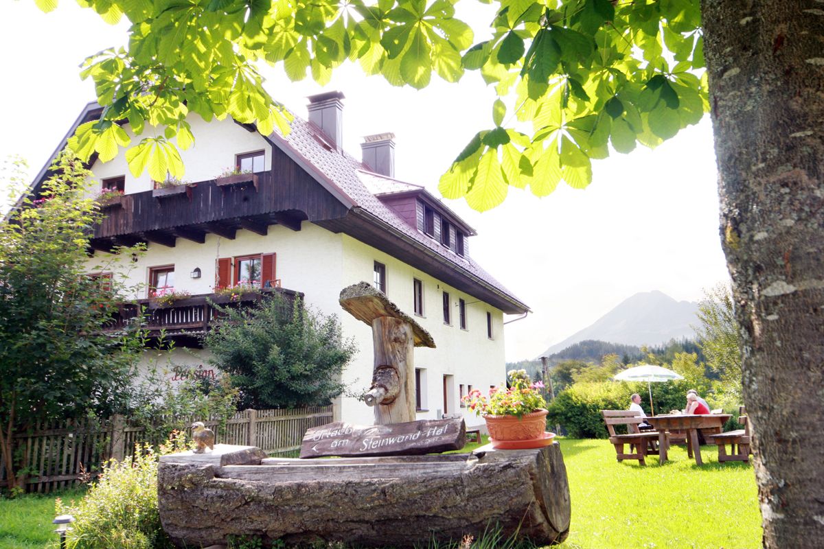 Ein traditionelles Bauernhaus mit Holzbalkon, umgeben von grüner Natur und einem Baum im Vordergrund.