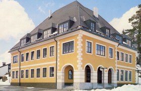 Gelbes Gebäude mit grauem Dach und vielen Fenstern, umgeben von Schnee.