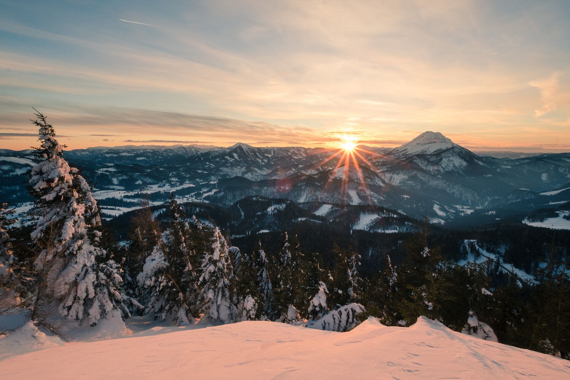 Die majestätischen Gipfel des Ötschers erheben sich stolz über die schneebedeckten Wälder, während die Sonne langsam hinter den Bergen versinkt. Ein atemberaubender Anblick, der die Herzen der Wanderer höher schlagen lässt und die unberührte Natur in ihrer vollen Pracht zeigt.