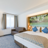 Modern hotel room with double bed, sofa and large mural with floral motif.