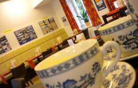 Innenansicht eines Caf&eacute;s mit Teetassen im Vordergrund und dekorierten W&auml;nden im Hintergrund.