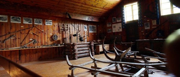 Innenansicht eines Museums mit Holzw&auml;nden, alten Werkzeugen und Schlitten.