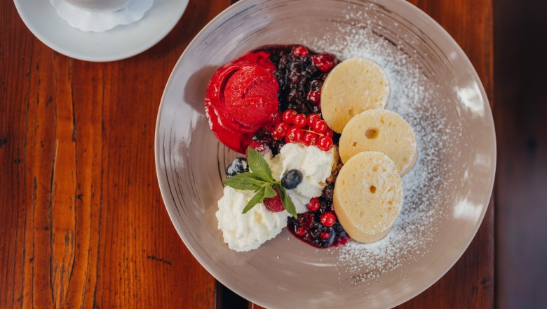 A dessert plate with semolina strudel, berry ragout, raspberry ice cream and whipped cream on a wooden table.
