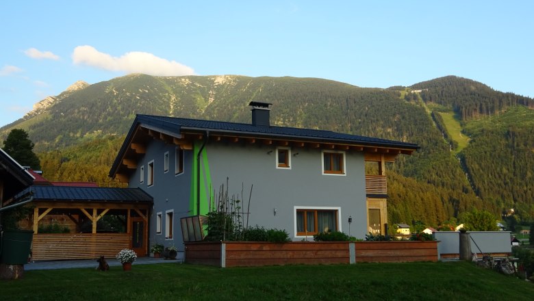 Ein modernes Haus mit grauer Fassade und Holzelementen vor einer Berglandschaft.