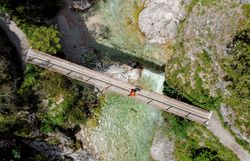 Ein malerischer Holzsteg führt über das glitzernde Wasser, umgeben von üppigem Grün und majestätischen Felsen. Die frische Bergluft und das sanfte Plätschern des Wassers laden zu einer Auszeit in der Natur ein. Hier, im Herzen des Naturparks, entfaltet sich die Schönheit der alpinen Landschaft in voller Pracht.