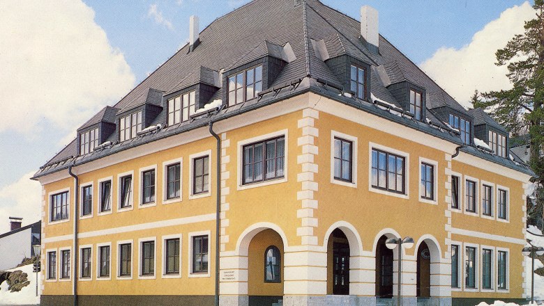 Gelbes Gebäude mit grauem Dach und vielen Fenstern, umgeben von Schnee.