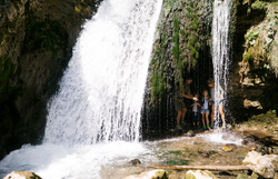 Ein erfrischender Wasserfall plätschert sanft über moosbedeckte Felsen, während eine Familie fröhlich im kühlen Nass spielt. Umgeben von üppigem Grün und der ruhigen Atmosphäre des Naturparks Ötscher Tormäuer, lädt dieser Ort zu unvergesslichen Momenten in der Natur ein.