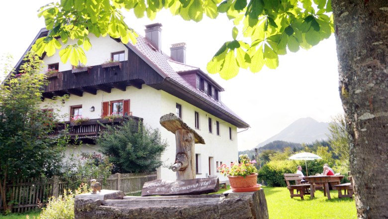Ein traditionelles Bauernhaus mit Holzbalkon, umgeben von grüner Natur und einem Baum im Vordergrund.