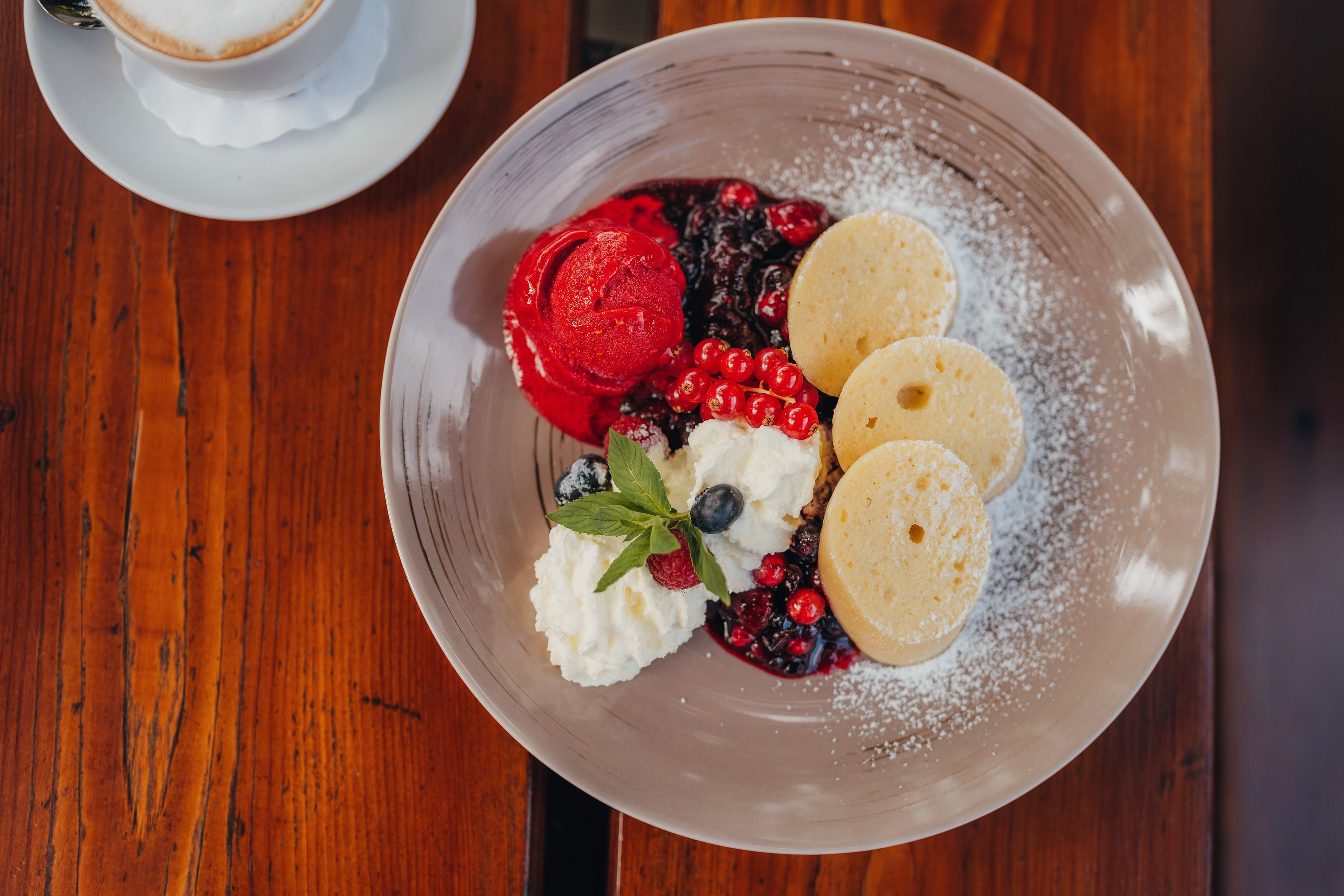 Ein Dessertteller mit Grießstrudel, Beerenragout, Himbeereis und Sahne auf einem Holztisch.