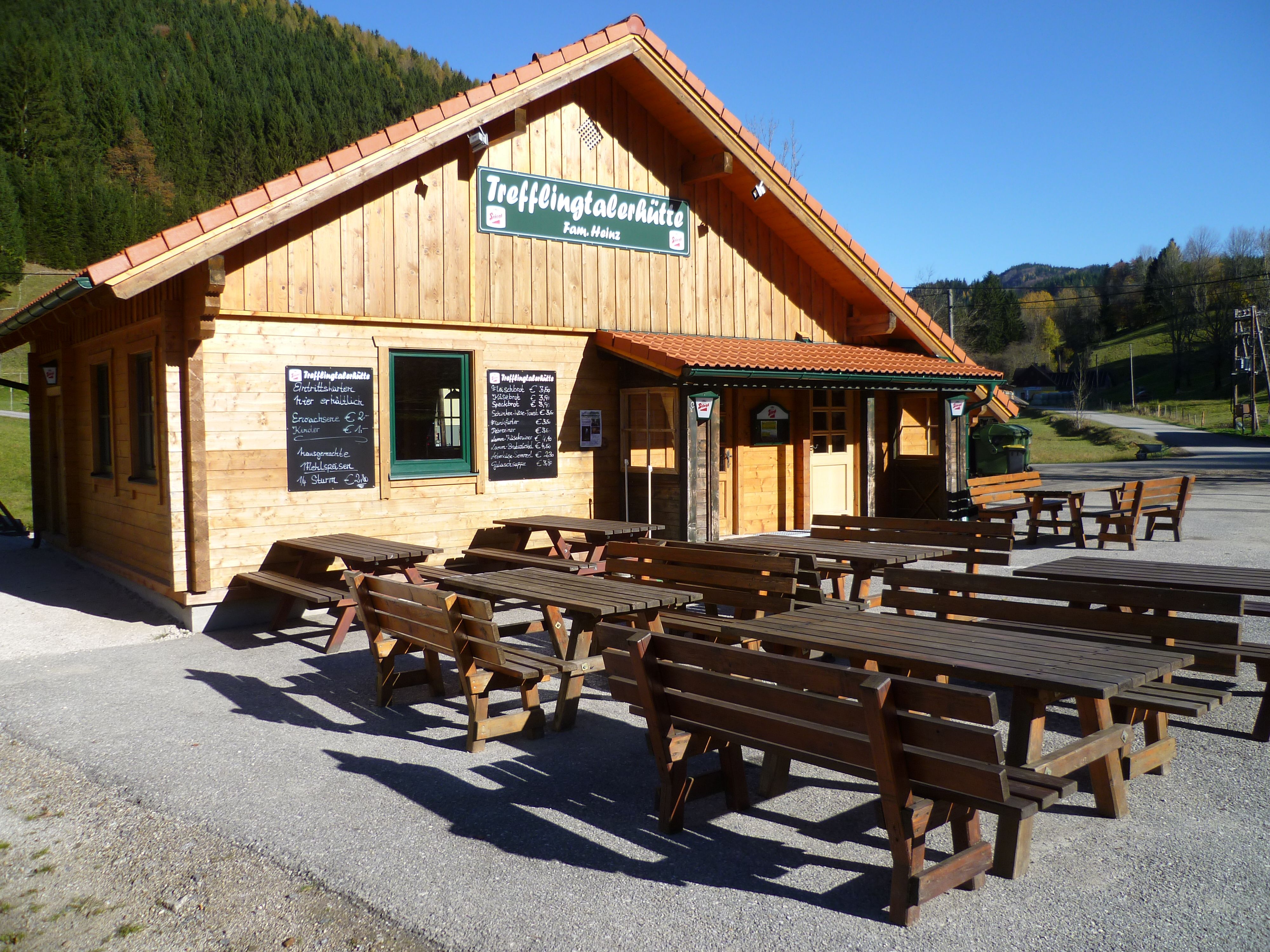 Holzhütte mit Tischen im Freien, sonniger Tag.