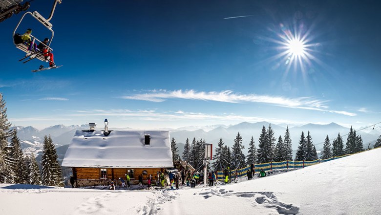 Winterlandschaft mit Skihütte, Sessellift und Bergen im Hintergrund.