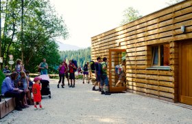 Menschen vor einem modernen Holzgebäude in einer Waldumgebung.