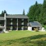 Hotel building with solar panels and green meadow in the foreground, surrounded by forest.