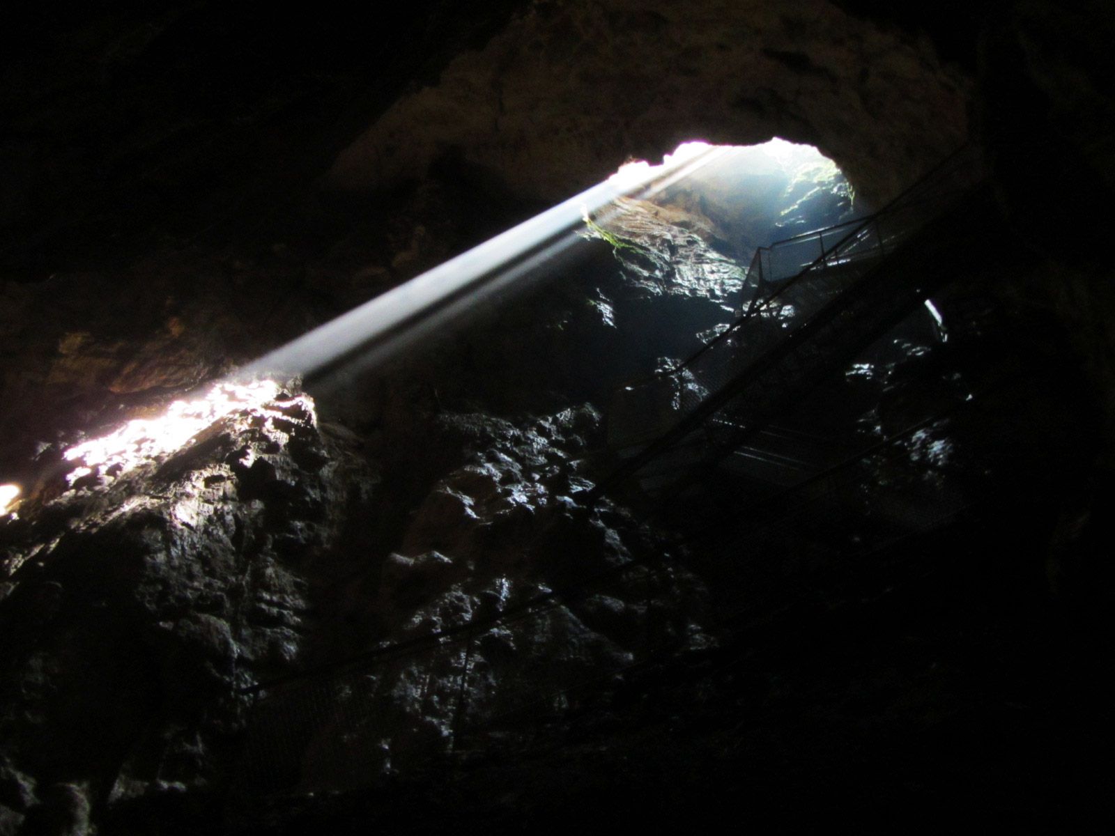 Sonnenstrahlen dringen durch eine Öffnung in einer dunklen Tropfsteinhöhle.