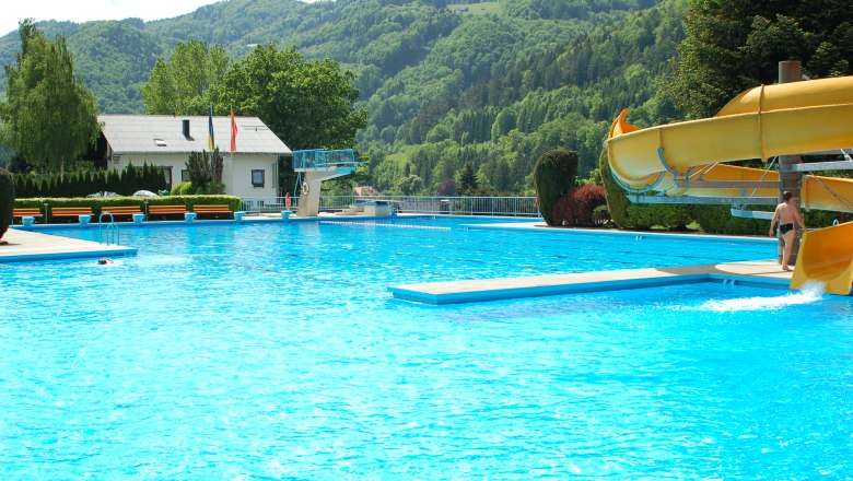 An outdoor pool with slide, diving board and surrounding mountains.