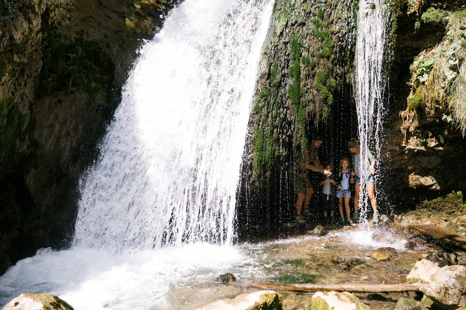 Ein erfrischender Wasserfall plätschert sanft über moosbedeckte Felsen, während eine Familie fröhlich im kühlen Nass spielt. Umgeben von üppigem Grün und der ruhigen Atmosphäre des Naturparks Ötscher Tormäuer, lädt dieser Ort zu unvergesslichen Momenten in der Natur ein.